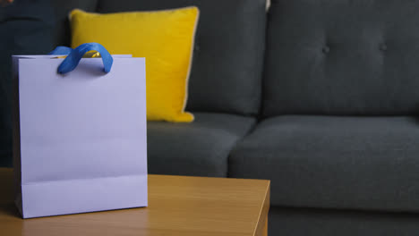 Close-Up-Of-Man-Picking-Up-Gift-Wrapped-Present-In-Bag-From-Table-In-Lounge-At-Home